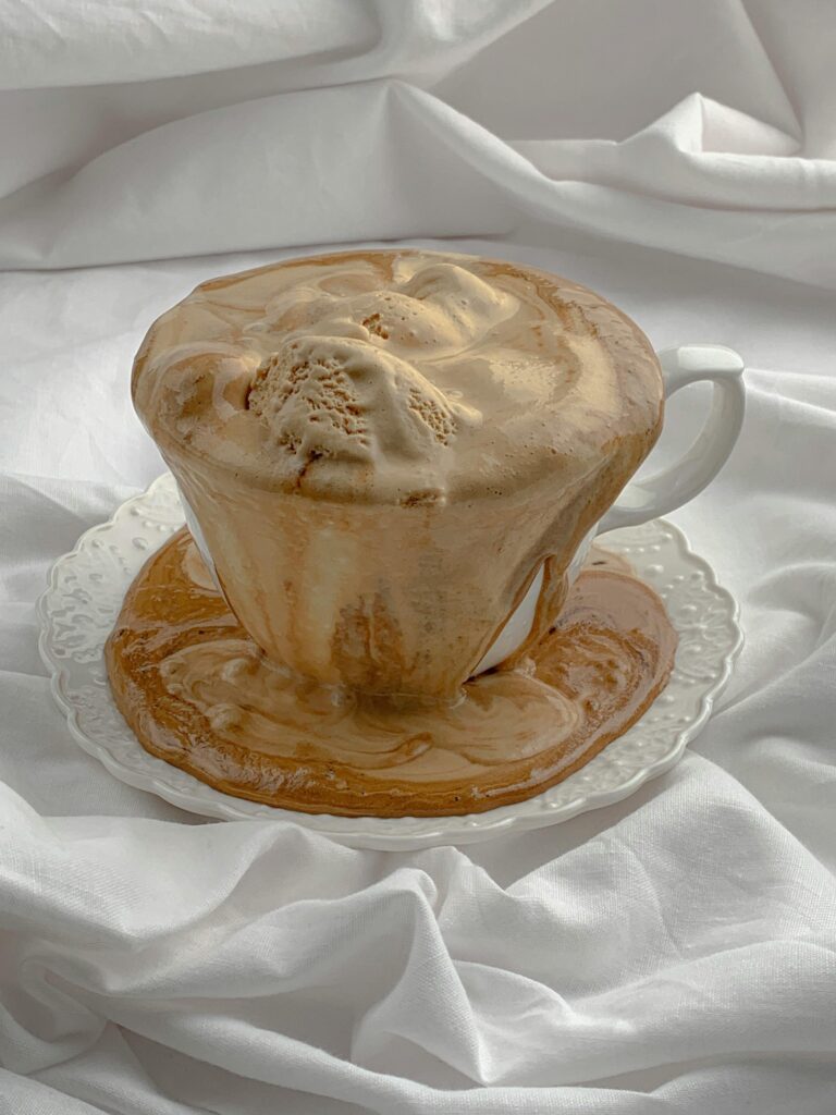 Delicious iced coffee with ice cream overflows a cup on elegant white fabric.