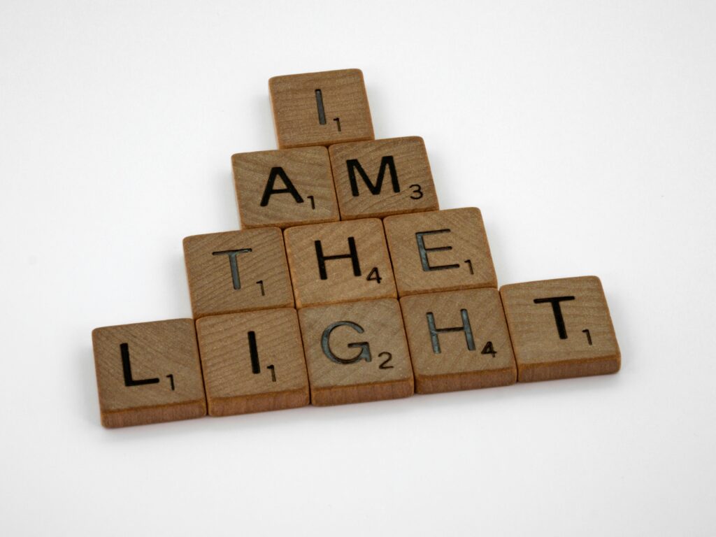 Wooden Scrabble tiles arranged to form the phrase 'I am the light' on a white surface.