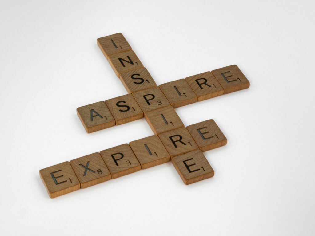 Wooden Scrabble tiles arranged to spell 'Inspire' and 'Expire' on a white surface.