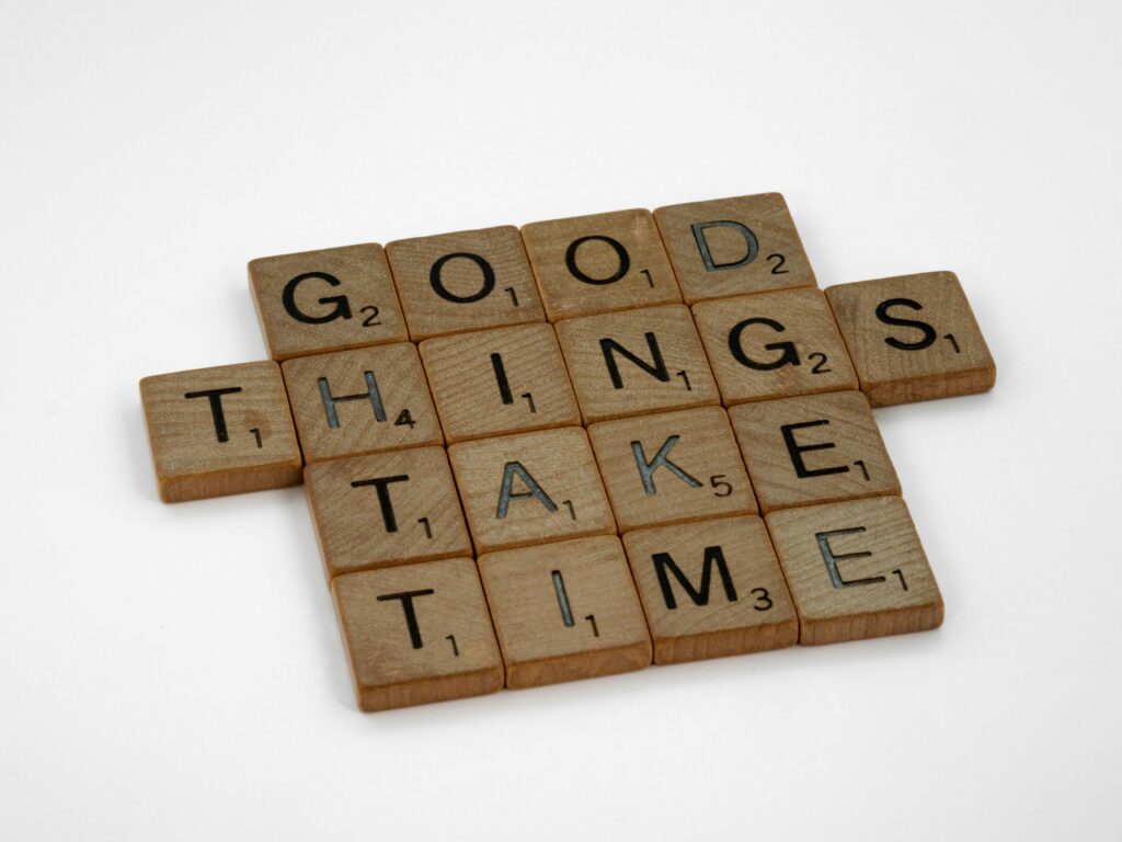 Close-up of wooden tiles spelling 'Good Things Take Time' on a white background.