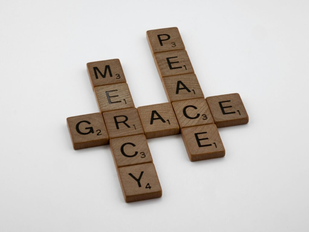 Wooden tiles spelling PEACE, MERCY, GRACE in crossword style on white background.