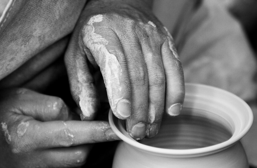 Artistic black and white close-up of hands shaping clay pottery on a wheel.