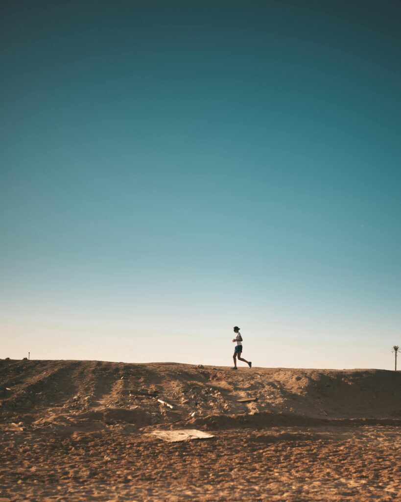 pexels-photo-1821694-1821694 A person jogs on a sandy path with a vast blue sky above, capturing movement and freedom.