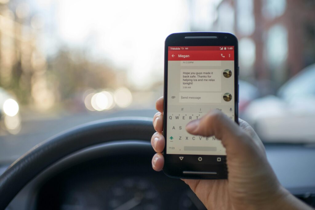 pexels-photo-230554-230554 Close-up of a person texting on a smartphone while driving a vehicle, highlighting distracted driving.