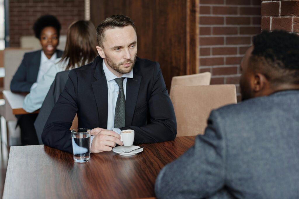 pexels-photo-4427910-4427910 Two businessmen in suits discussing over coffee during a meeting in a café.