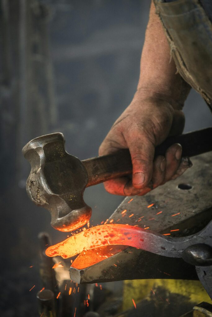 pexels-photo-3680094-3680094 Close-up of a blacksmith hammering a hot iron piece in a workshop.