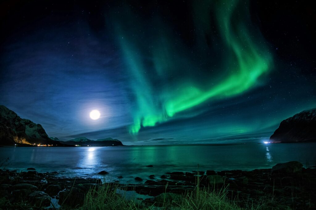 pexels-photo-5421888-5421888 Scenic view of glowing sun with aurora in sky reflecting in sea near mountains at dusk