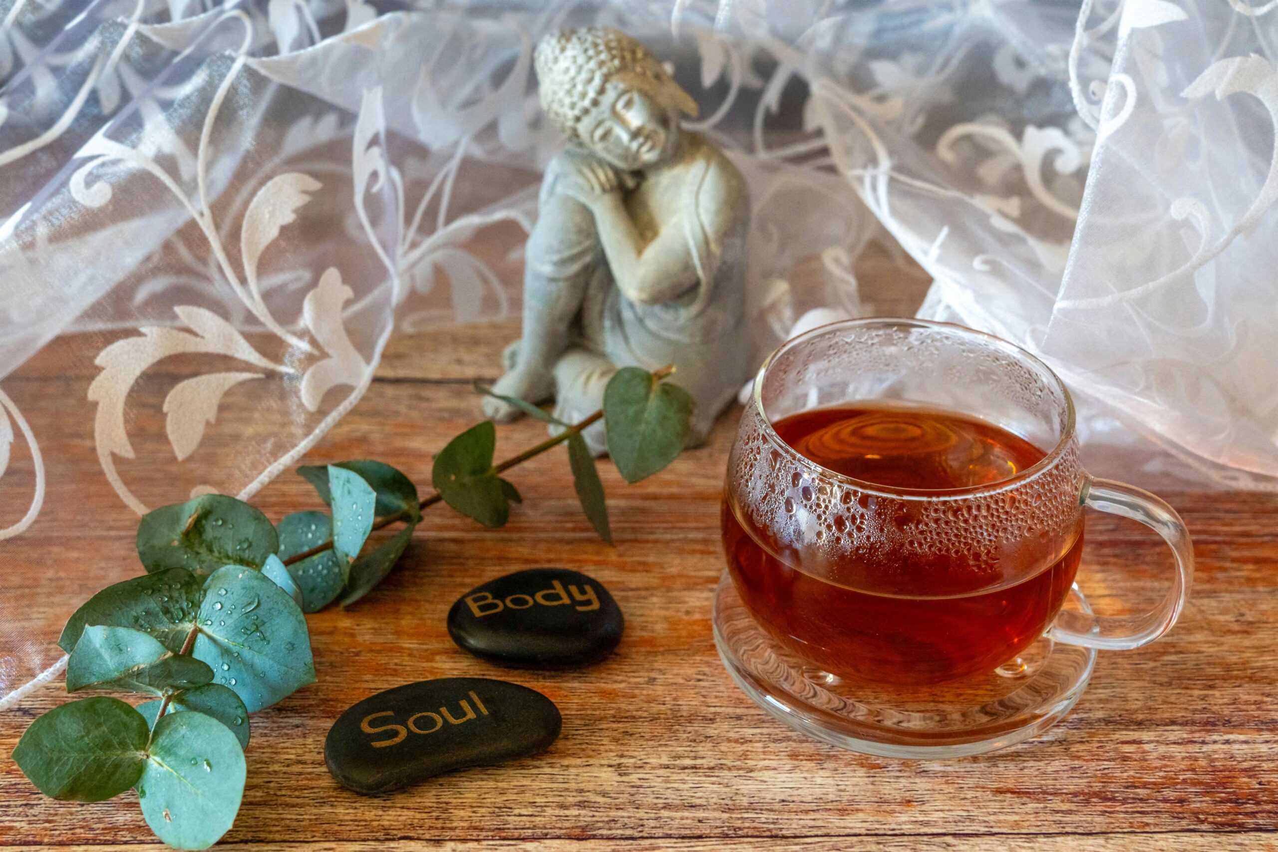 A calming tea arrangement featuring a Buddha statue, leaf sprig, and stones labeled 'Body' and 'Soul.'