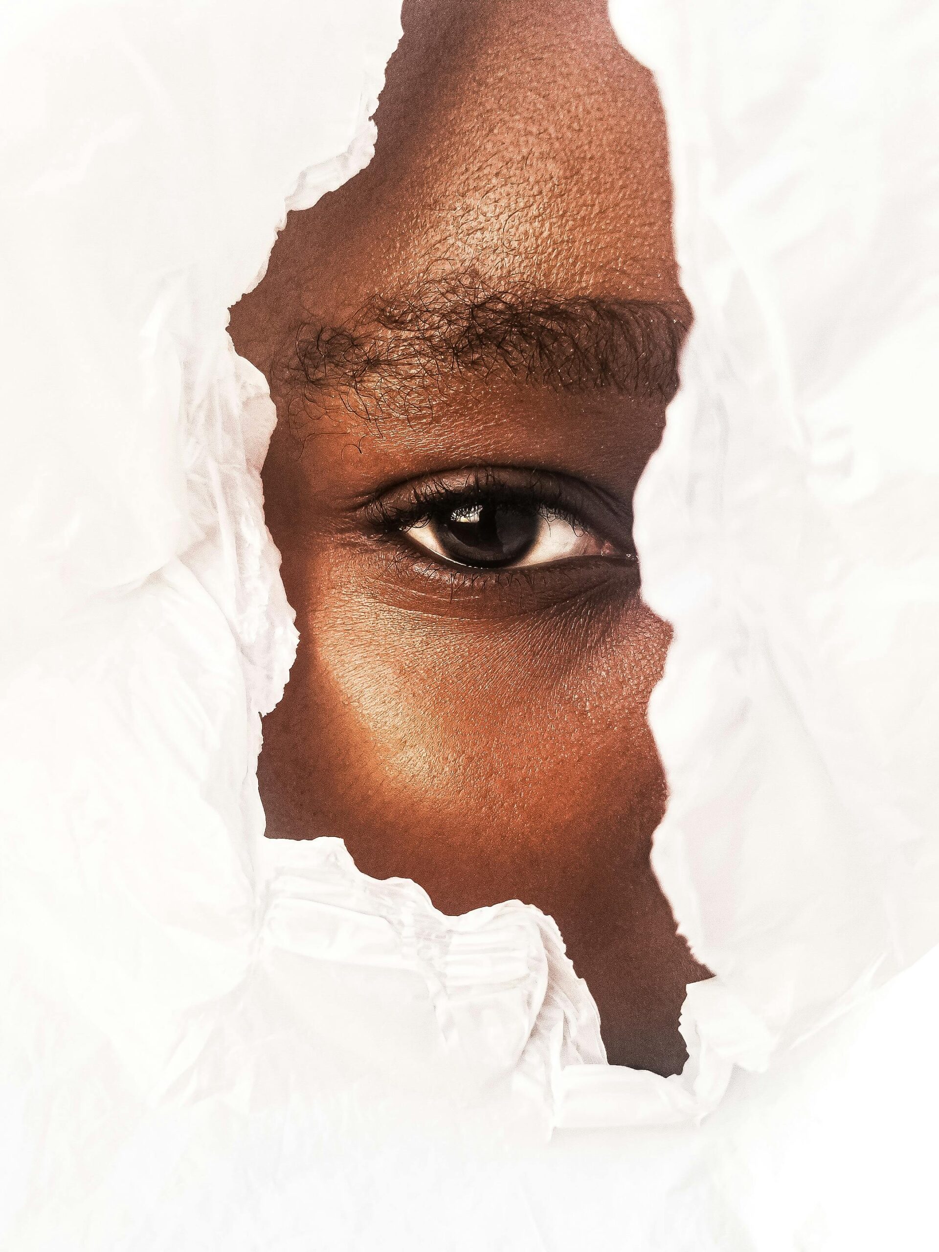 Close-up of an eye peeking through a torn white paper background.