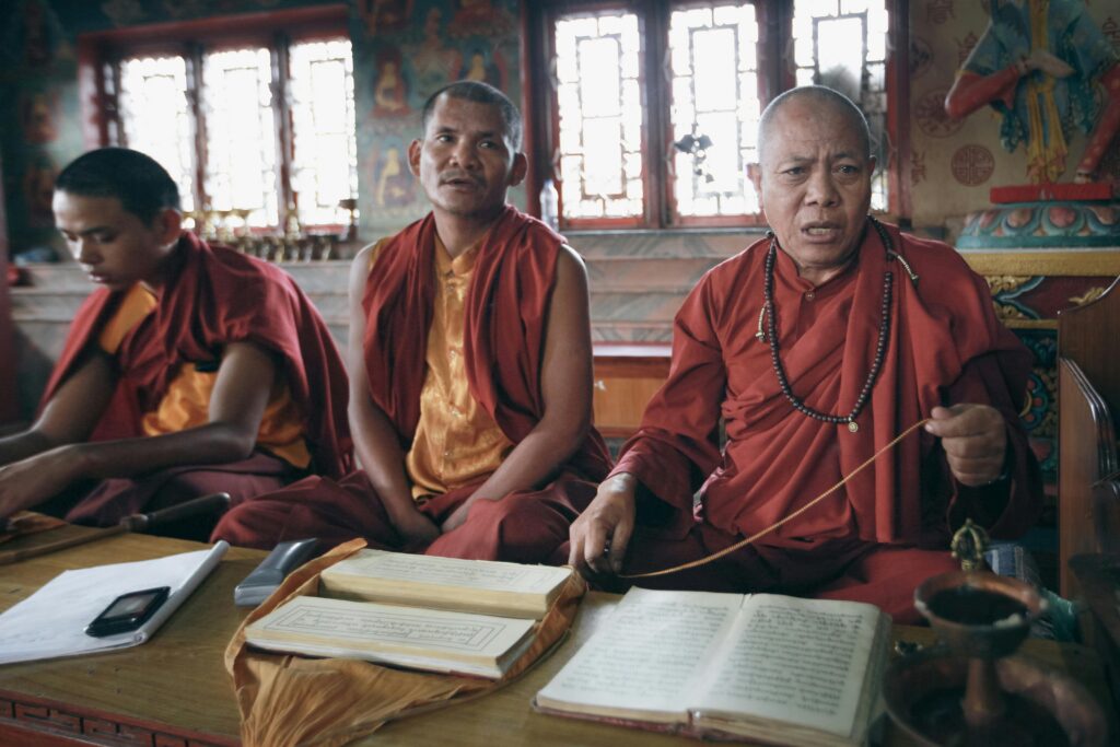 Buddhist monks engaged in focused prayer inside a traditional monastery setting.