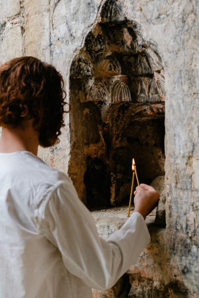 A man lights a candle in a stone alcove, capturing a moment of spiritual reflection.
