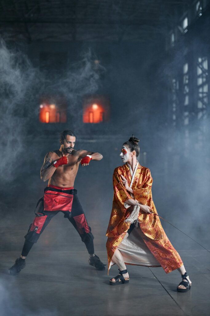 Two cosplayers in intense martial arts battle amid dramatic fog.