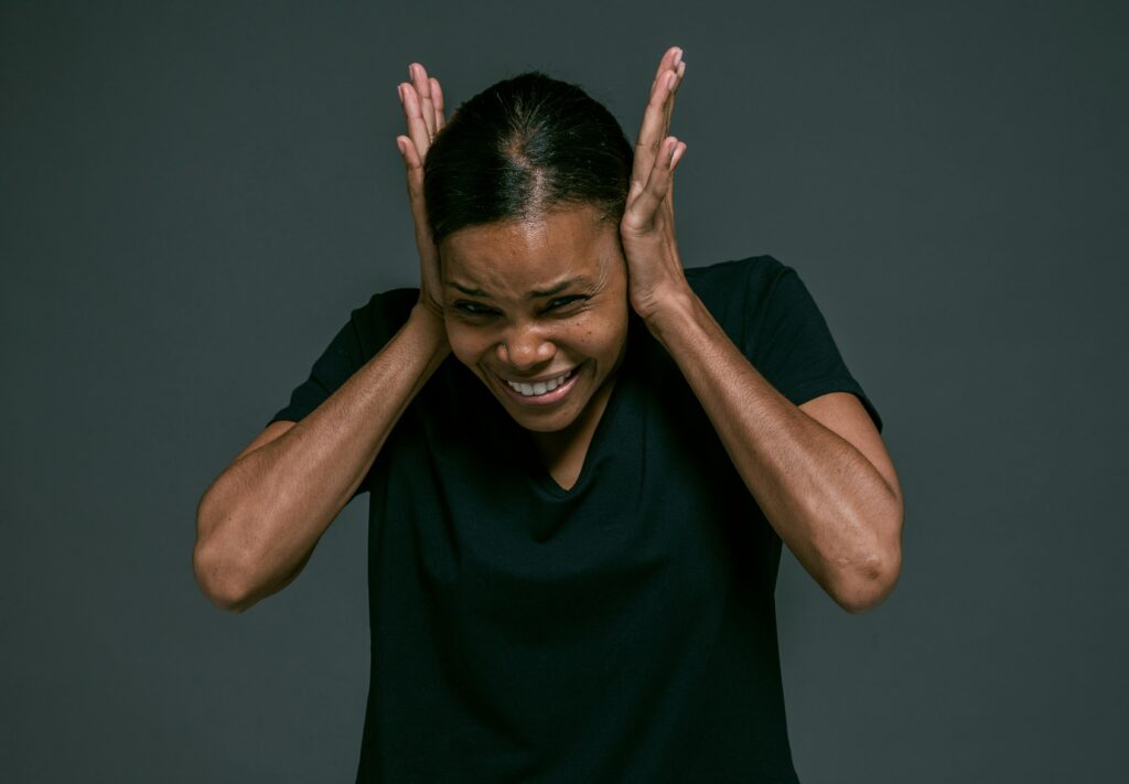 Portrait of an adult woman covering ears, looking irritated, against a dark background.