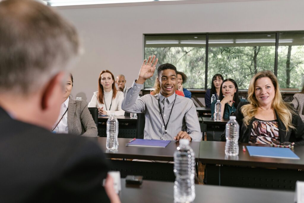 Businesspeople in a conference room engaging in a discussion, with a man raising his hand.