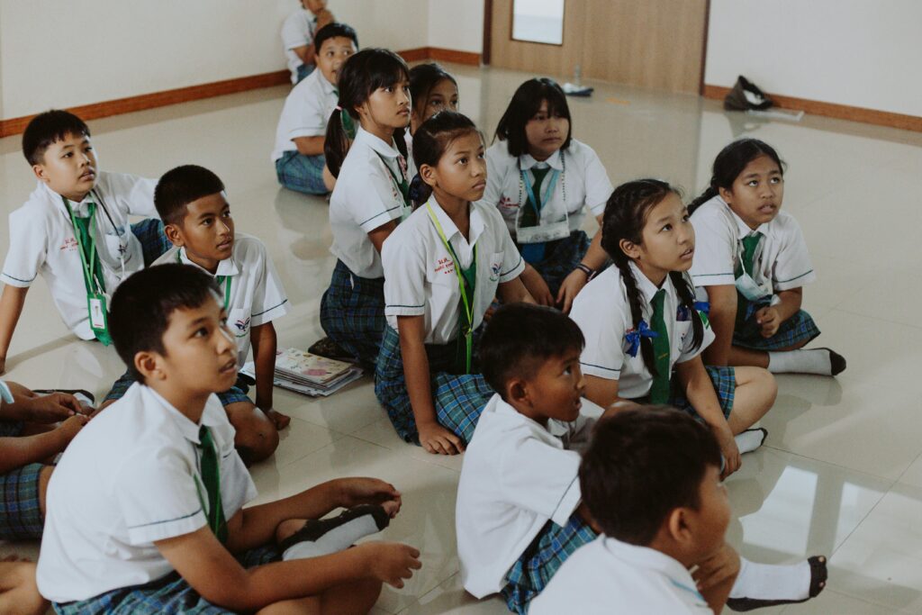 Children in school uniforms attentively listening in an indoor classroom setting.