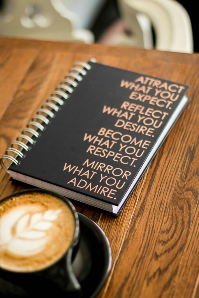 A notebook with motivational quotes next to a coffee cup on a wooden table.