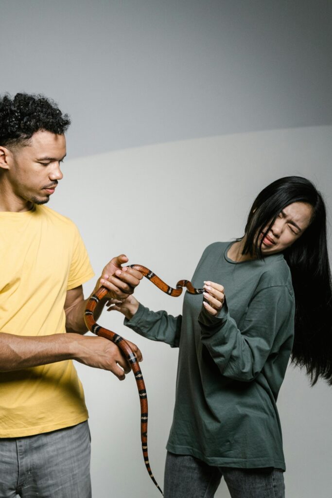 A man and woman holding a snake showing mixed expressions, illustrating phobia and curiosity.