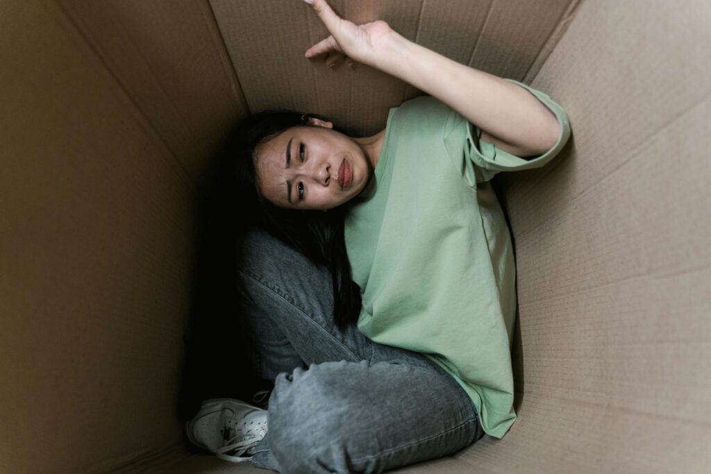 Woman enclosed in a cardboard box, showing signs of stress and fear.